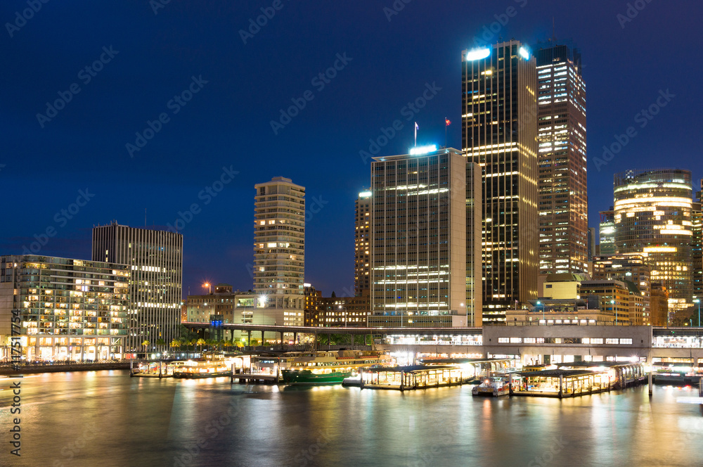 Obraz premium Modern cityscape at night. Circular Quay skyscrapers and hotels with ferry wharfs in the evening. Sydney, Australia