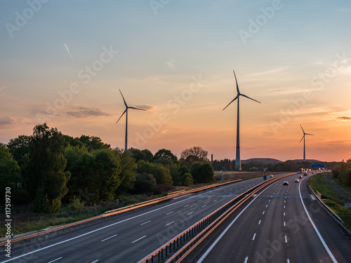 sunset over a highway, wind turbines in the background