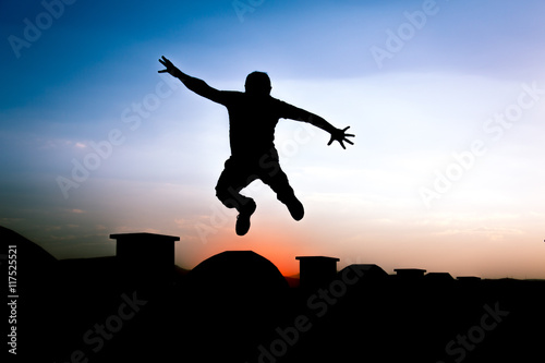 Defocused Silhouette of a boy is jumping over beautiful sunset background.