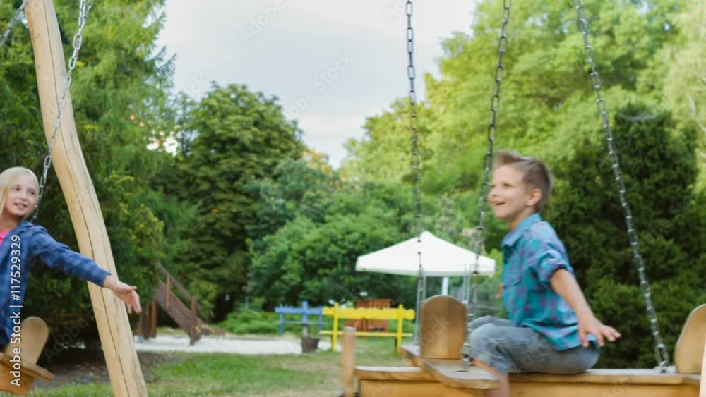 Smiling boy and girl having fun at playground. Children playing outdoors in summer. Teenagers riding on a swing outside Smiling boy and girl having fun at playground. Children playing outdoors in summer. Teenagers riding on a swing outside