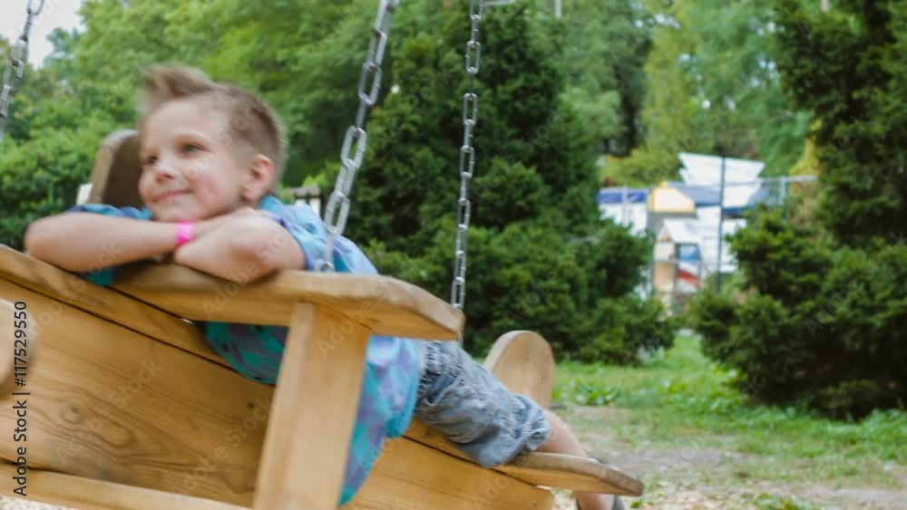 Smiling boy having fun at playground. Child playing outdoors in summer. Teenager riding on a swing outside Smiling boy having fun at playground. Child playing outdoors in summer. Teenager riding on a swing outside