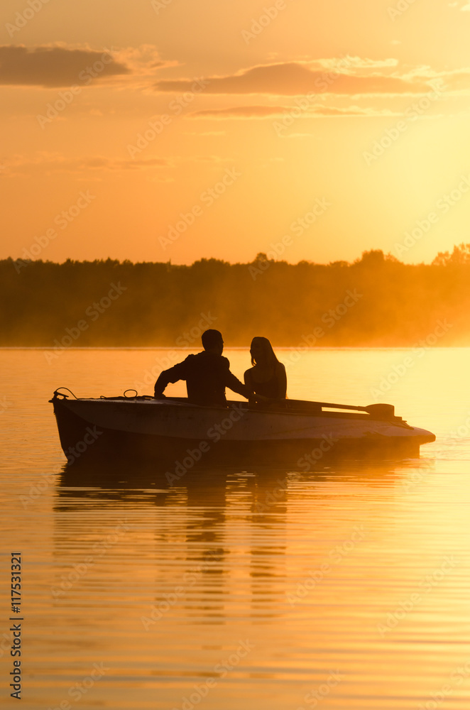 Romantic golden river sunset. Couple on boat backlit by sunlight