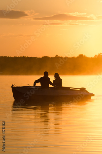 Romantic golden river sunset. Couple on boat backlit by sunlight