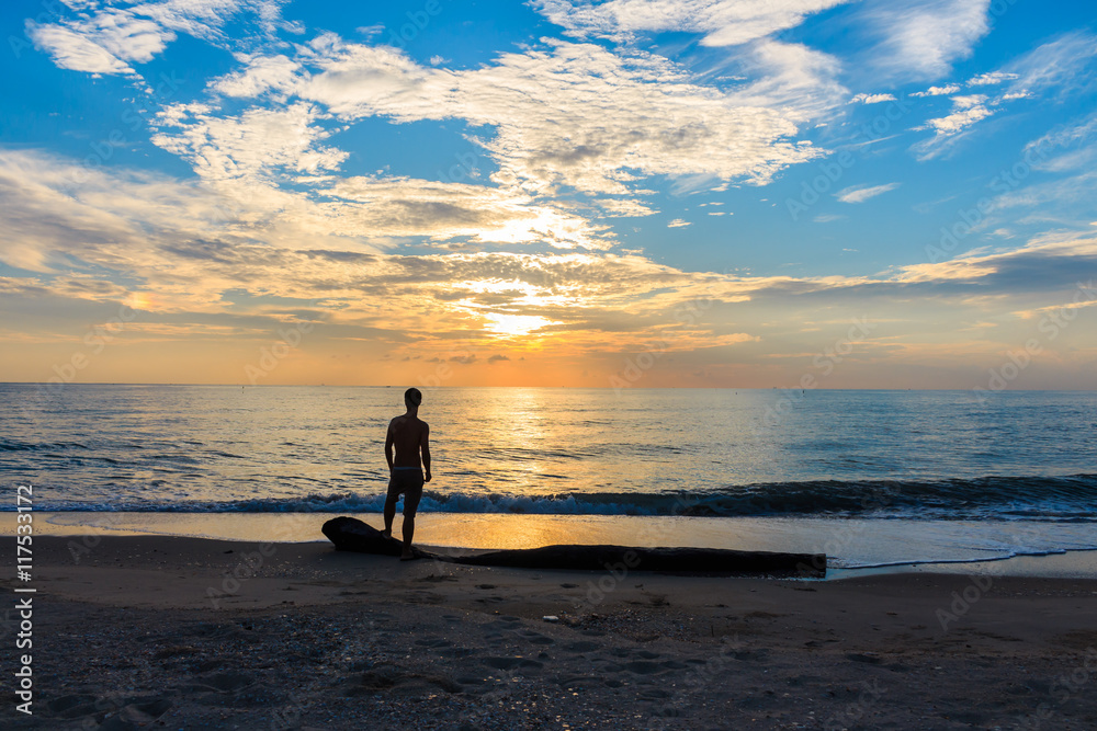 Man standing on the beach watching the sunrise.