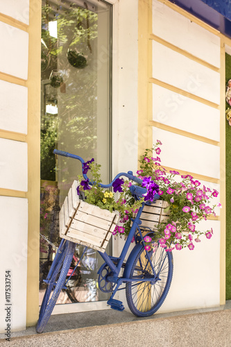 Fototapeta Naklejka Na Ścianę i Meble -  Old painted blue color bicycle with flowers as an ornament, leaning against the house wall