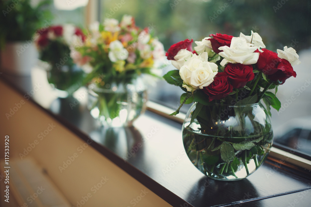 Red and white roses in glass bowls stand on the black windowsil Red and white roses in glass bowls stand on the black windowsil