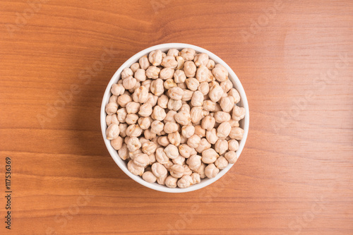 Raw Chickpeas into a spoon over a wooden table. 
