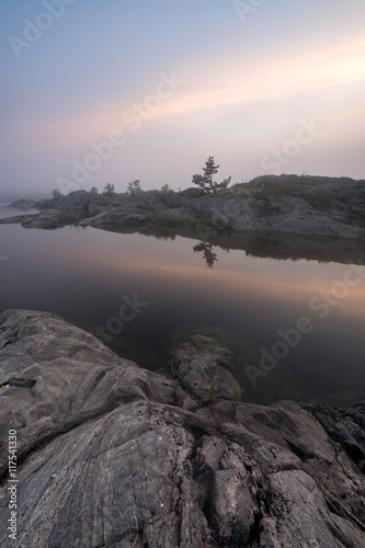 First rays of a new day illuminated front of fog and reflected in the still water of Ladoga lake, Russia 