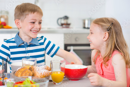 Two happy children having breakfast in kitchen