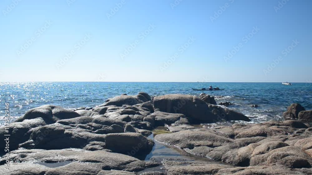 Canoe crossing the blue sea whose waves crashing on the shore rocks. Canoe crossing the blue sea whose waves crashing on the shore rocks.