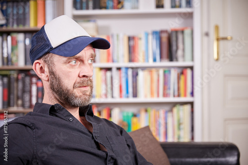 Man with beard and baseball cap sitting in a library