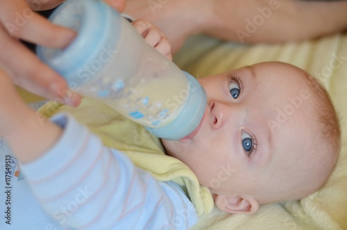 Baby is drinking infant milk from the bottle which parent´s hand holds.
