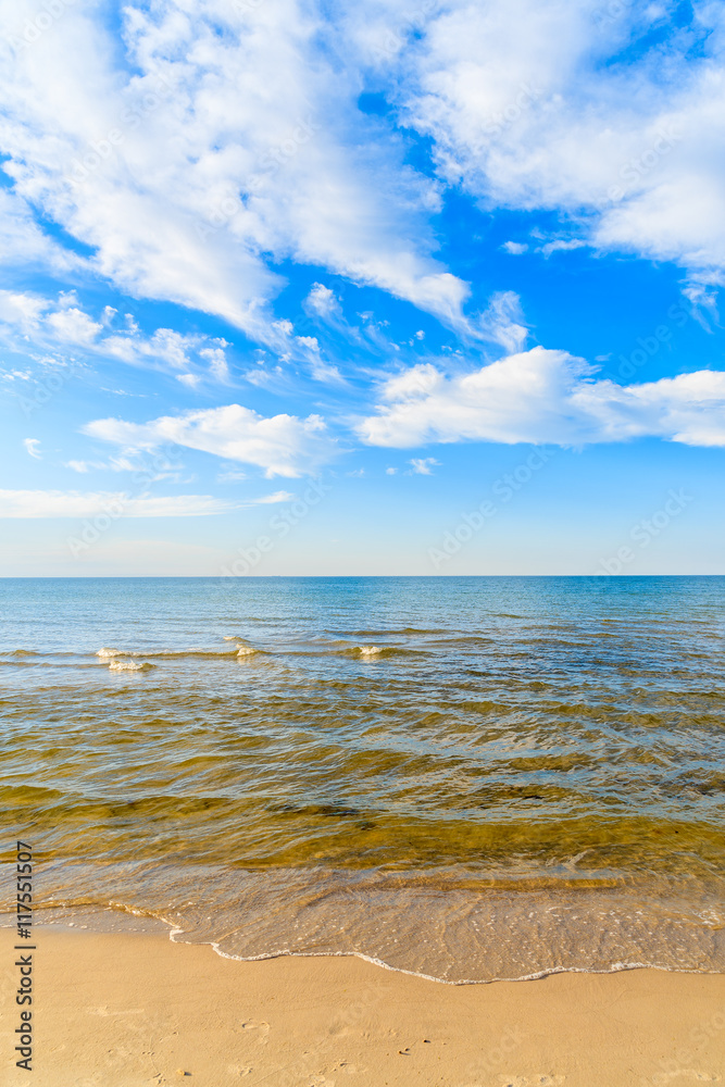 Sea waves on sandy beach and white sunny clouds on blue sky in Debki village, Baltic Sea, Poland
