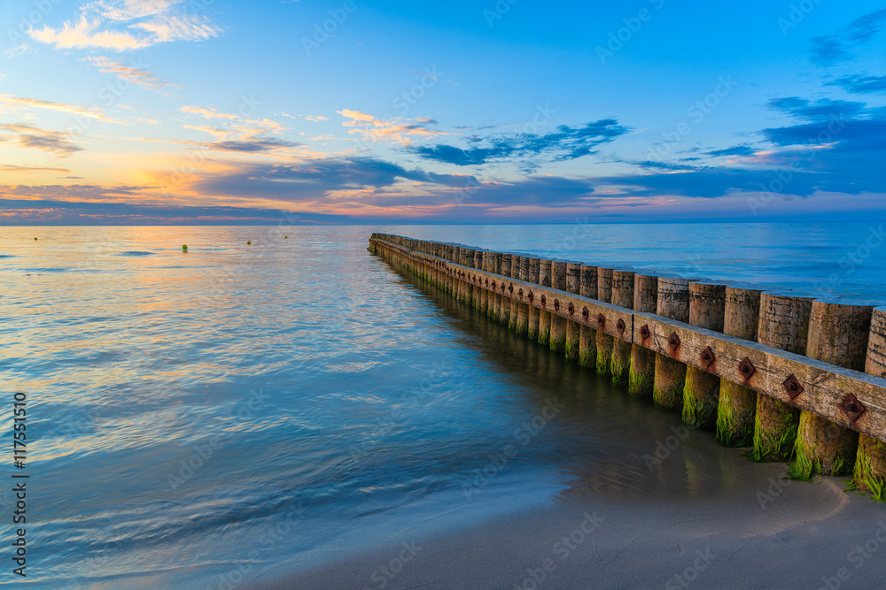 Sunset on beach with a wooden breakwater in Leba, Baltic Sea, Poland Sunset on beach with a wooden breakwater in Leba, Baltic Sea, Poland