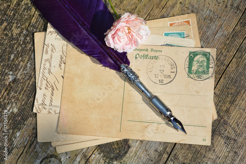 alte leere Vintage Postkarte mit alter Briefmarke liegt auf altem Holz mit Rose und Schreibfeder photo