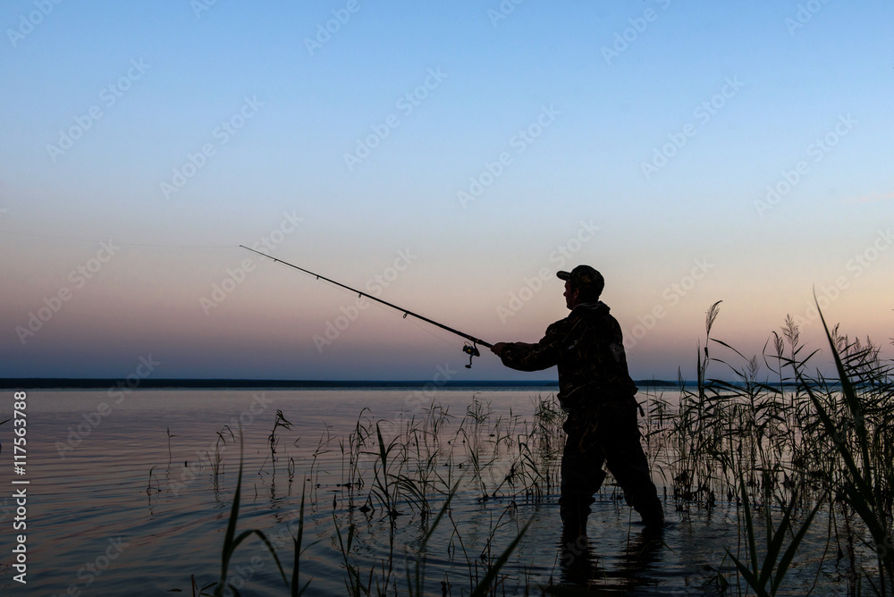 Fisherman silhouette at sunset on the lake while fishing
