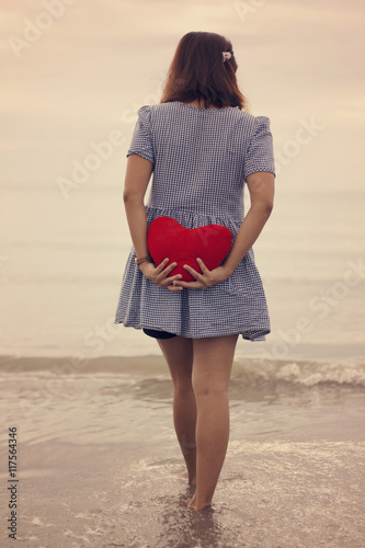 Woman holding a red heart on the beach