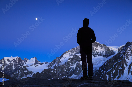 Mountaineer looking at the moon rising above the mountains in Wallis, Switserland.