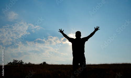 Silhouette of man worship with hands raised to the sky in nature