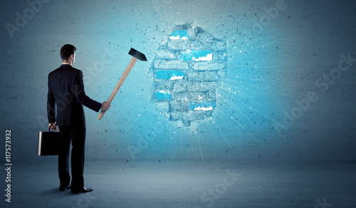 Business man hitting brick wall with huge hammer