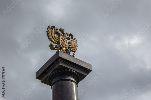 Золотой герб Российской Федерации крупным планом на стелле на фоне облаков/
