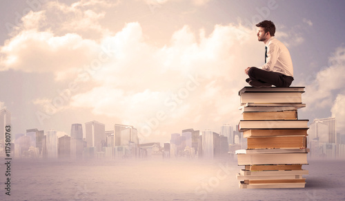 Man sitting on pile of books above city