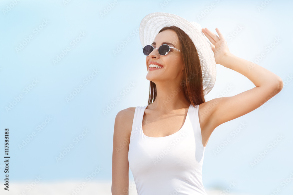 Beautiful young woman in glasses holding hat on the beach. Summer holidays and vacation concept. Beautiful young woman in glasses holding hat on the beach. Summer holidays and vacation concept.