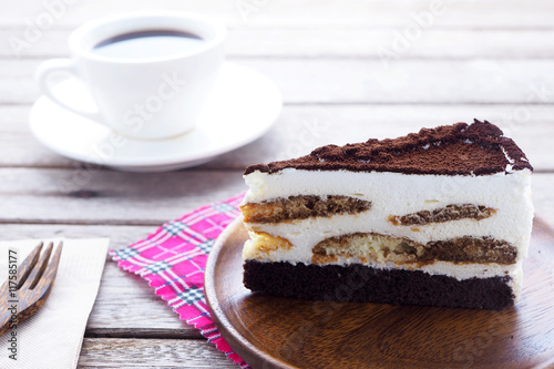 Close up of Tiramisu cake on a wooden plate with coffee.