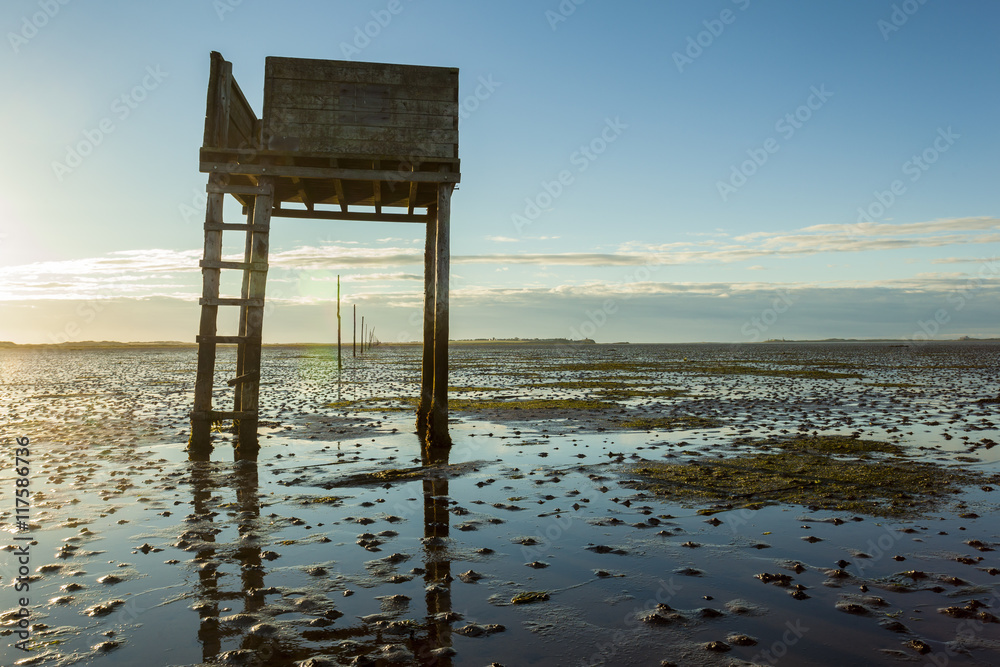 Safety and refuge shelter on foot path, cuasway to Holy Island and Lindisfarne Priory, Northumberland, England, UK. At sunrise with early morning sunlight and reflections in the water.