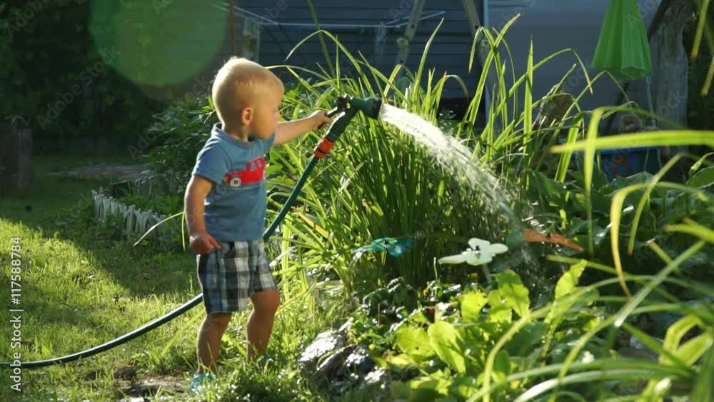 Funny little boy 1.5 years studying hosing plants in the garden