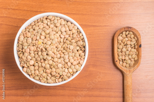 Raw Lentils into a bowl and spoon over a wooden table. (Lens cul