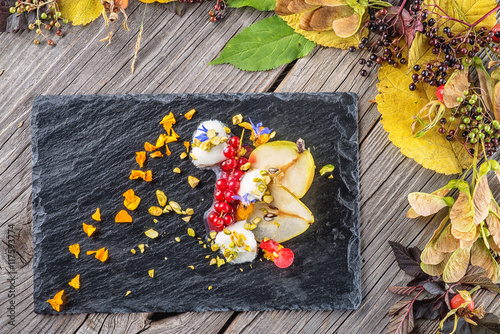exclusive autumn cream dessert with pears, currants and pistachios on black board, decorated with flowers petals, product photography for restaurant