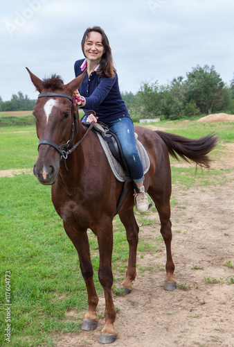Joyful young woman touching her chestnut horse while riding on field