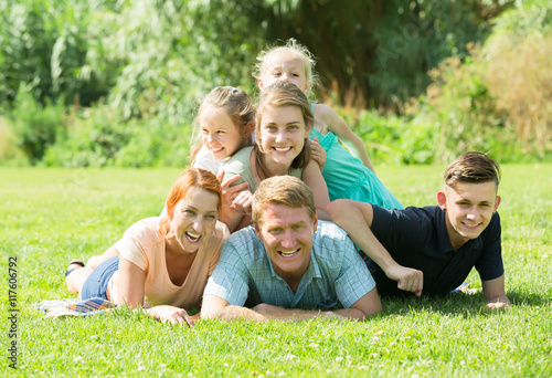 Portrait of big vigorous family lying together on green lawn out