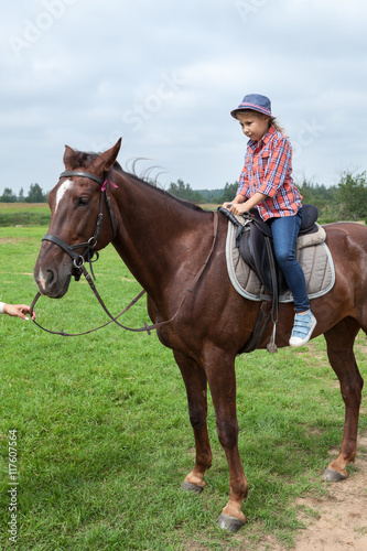 Young girl riding horse with instructor help