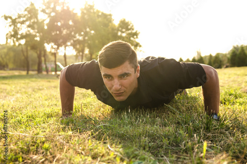 Close up of a man doing pushups on the grass with the horizon in the background. © valerii kalantai