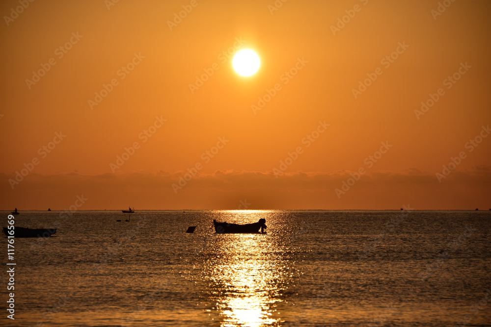 Alba con sole rosso e silhouette di barca