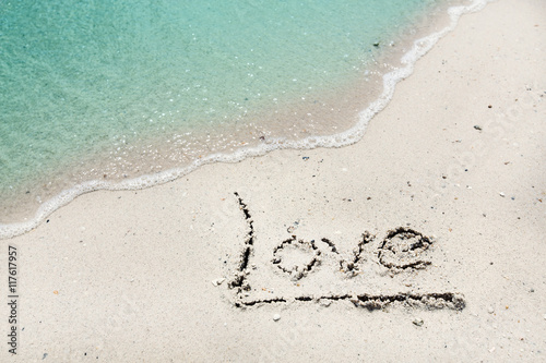 Word Love handwritten on sandy beach with soft ocean wave on background