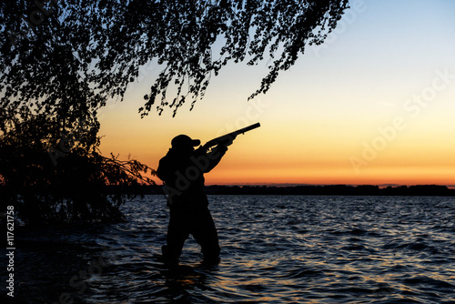 Hunter silhouette at sunset, while hunting on the lake 