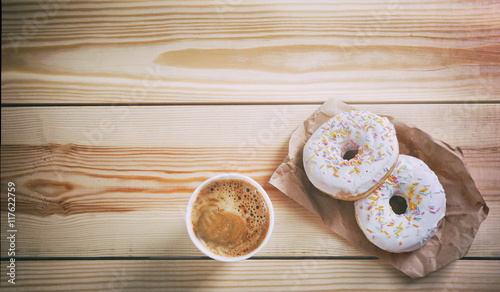 Paper cup of coffee and doughnuts on wooden background