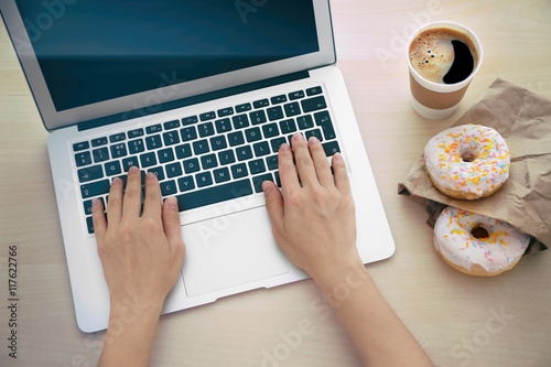 Female hands with laptop and cup of coffee on wooden background