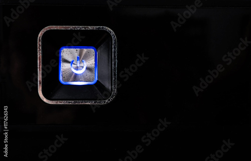 Old rusty power button with blue light on black metallic background photo