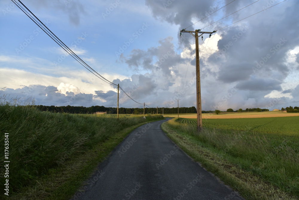 Route de campagne sous la lumière du soir contrastant avec les nuages gris après le passage d'un front froid au Périgord Vert