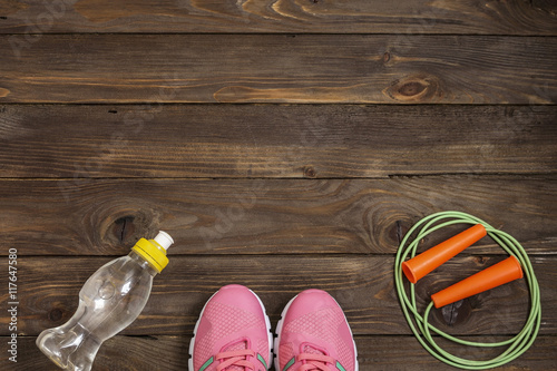 Sport shoes, skipping rope and water bottle on wooden background. Sport, diet and healthy lifestyle concept. Clothing and sports accessories for fitness. The view from the top. The place to advertise.