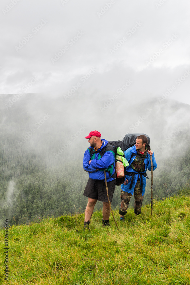 Two tourists looking at the landscape of the Carpathian mountains, summertime journey
