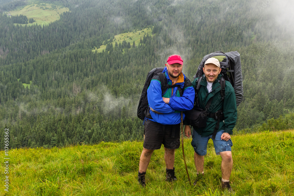 Portrait of two man hikers with backpacks in Carpathian mountains, summertime journey