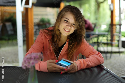 Uśmiechnięta dziewczyna z telefonem przy stoliku w restauracji.