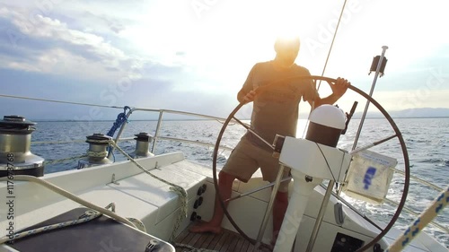 man on steering wheel navigating sail boat