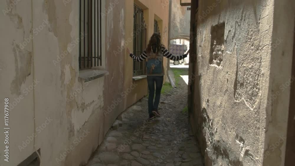 Lady walks between buildings. Woman is touching old walls. History draws people. Travel through the city continues. Lady walks between buildings. Woman is touching old walls. History draws people. Travel through the city continues.
