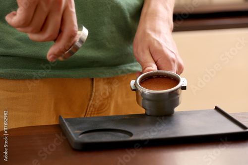 Barista pressing ground coffee with tamper in portafilter